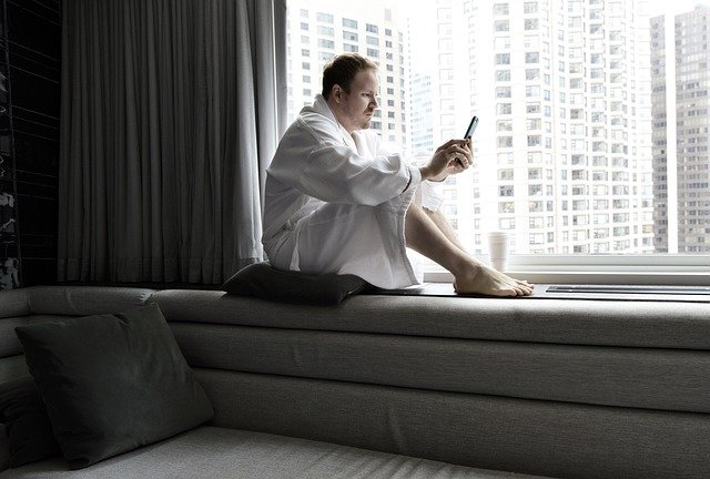 whatsapp marketing for hotel - man by the hotel window wearing bathrobe and using smartphone